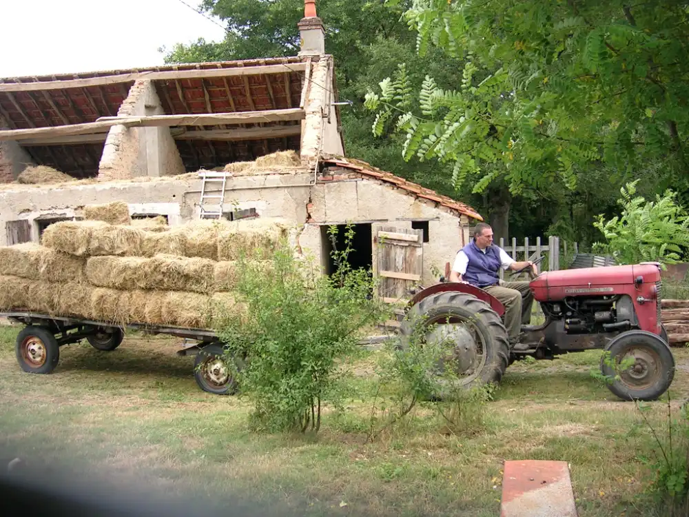 tractor met een wagen vol hooi rijdt langs de oude boerderij