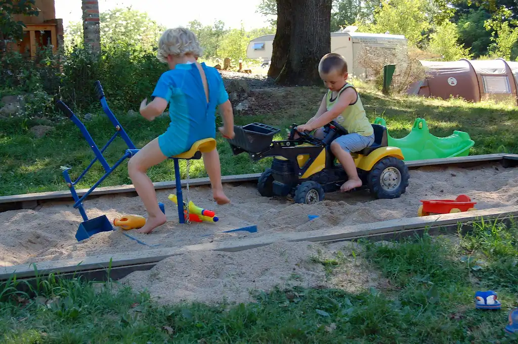 twee kinderen in een zandbak op graafmachines aan het spelen