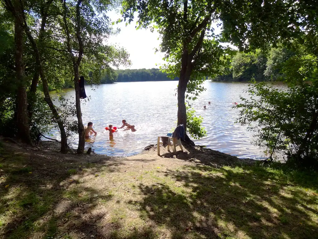 Zicht op het meer tussen de bomen door. Mensen spelen in het water